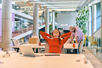 Image showing In a modern startup office, a professional businesswoman with orange hair sitting at her laptop and resting on job break