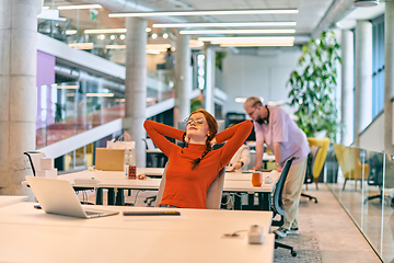 Image showing In a modern startup office, a professional businesswoman with orange hair sitting at her laptop and resting on job break