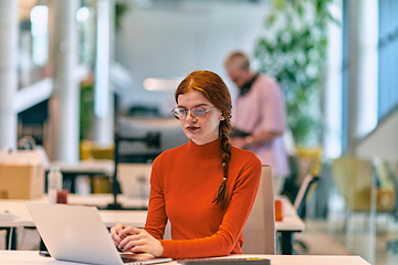 Image showing In a modern startup office, a professional businesswoman with orange hair sitting at her laptop, epitomizing innovation and productivity in her contemporary workspace.