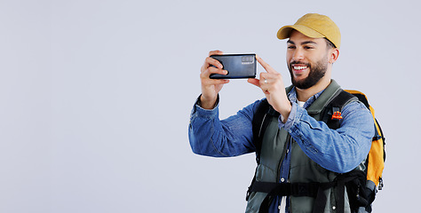 Image showing Hiking, backpack and happy man with phone in studio for video call, photography or memory on grey background. Travel, smartphone and male backpacker with app for live streaming journey in nature