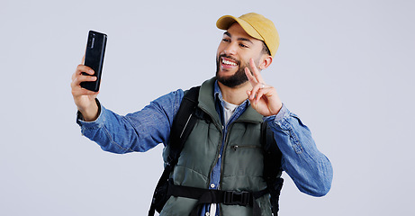 Image showing Hiking, smile and man with selfie, peace sign and social media with fun on white studio background. Person, model and hiker with a smartphone, profile picture and adventure with blog, journey or post