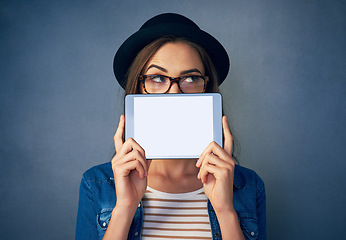 Image showing Face, tablet and space with a fashion woman in studio on a blue background for social media marketing. Idea, display and style with a young person holding an empty screen for advertising mockup