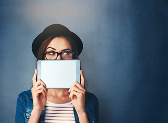 Image showing Face, tablet screen and mockup with a fashion woman in studio on a blue background for social media marketing. Thinking, display and style with a young person holding empty tech for advertising space