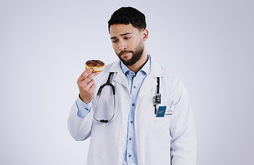 Image showing Doctor, diet and thinking with donut in hand for nutrition in studio, white background or mockup space. Nutritionist, choice and man with doubt or decision for health with dessert, sweets or candy