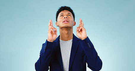 Image showing Man, fingers crossed or good luck in studio for prize, promotion or competition giveaway by blue background. Model, hope and emoji for wish for blessing, nervous and waiting for results in mockup