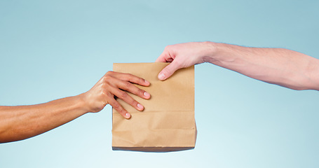 Image showing Hands, paper bag and delivery in studio closeup for fast food, supply chain and cargo by blue background. Courier, logistics and package for service, shipping and giving to customer for e commerce