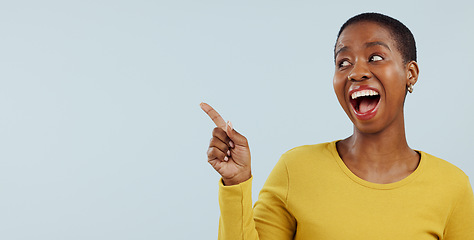 Image showing Happy black woman, pointing and surprise for advertising or marketing against a gray studio background. Face of excited African female person smile in wow deal, sale promotion or discount on mockup