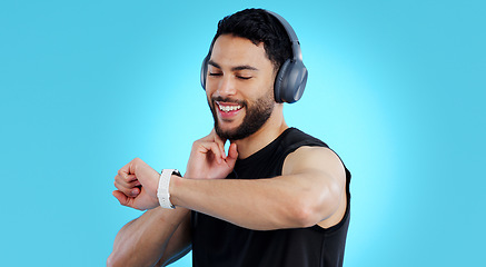 Image showing Happy man, headphones and checking watch for pulse in fitness against a blue studio background. Male person, athlete or model looking at wristwatch for monitoring performance or heart rate on mockup