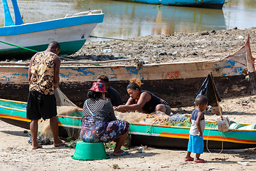 Image showing Fisherman and woman repairing fishing nets at the estuaries of a river. The woman has a traditionally Malagasy painted face