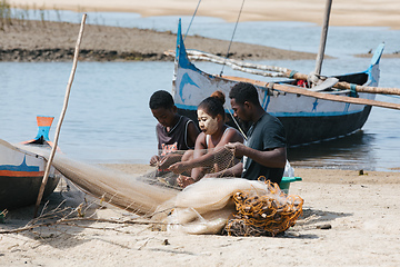 Image showing Fisherman and woman repairing fishing nets at the estuaries of a river. The woman has a traditionally Malagasy painted face