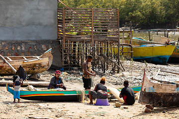 Image showing Fisherman and woman repairing fishing nets at the estuaries of a river. The woman has a traditionally Malagasy painted face