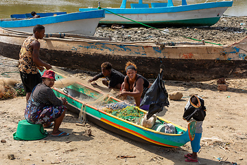 Image showing Fisherman and woman repairing fishing nets at the estuaries of a river. The woman has a traditionally Malagasy painted face