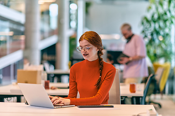 Image showing In a modern startup office, a professional businesswoman with orange hair sitting at her laptop, epitomizing innovation and productivity in her contemporary workspace.