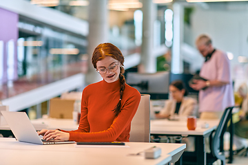 Image showing In a modern startup office, a professional businesswoman with orange hair sitting at her laptop, epitomizing innovation and productivity in her contemporary workspace.