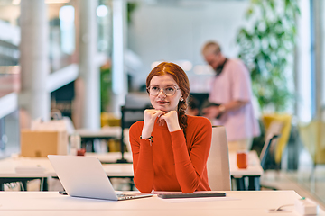 Image showing In a modern startup office, a professional businesswoman with orange hair sitting at her laptop, epitomizing innovation and productivity in her contemporary workspace.