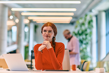 Image showing In a modern startup office, a professional businesswoman with orange hair sitting at her laptop, epitomizing innovation and productivity in her contemporary workspace.