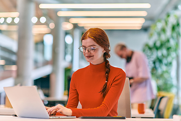 Image showing In a modern startup office, a professional businesswoman with orange hair sitting at her laptop, epitomizing innovation and productivity in her contemporary workspace.