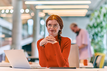 Image showing In a modern startup office, a professional businesswoman with orange hair sitting at her laptop, epitomizing innovation and productivity in her contemporary workspace.