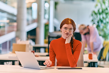 Image showing In a modern startup office, a professional businesswoman with orange hair sitting at her laptop, epitomizing innovation and productivity in her contemporary workspace.