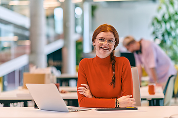 Image showing In a modern startup office, a professional businesswoman with orange hair sitting at her laptop, epitomizing innovation and productivity in her contemporary workspace.