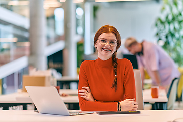 Image showing In a modern startup office, a professional businesswoman with orange hair sitting at her laptop, epitomizing innovation and productivity in her contemporary workspace.