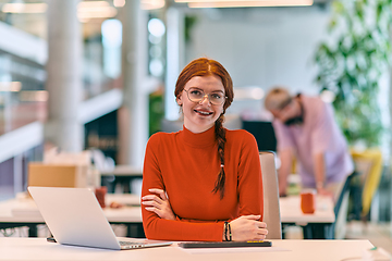 Image showing In a modern startup office, a professional businesswoman with orange hair sitting at her laptop, epitomizing innovation and productivity in her contemporary workspace.