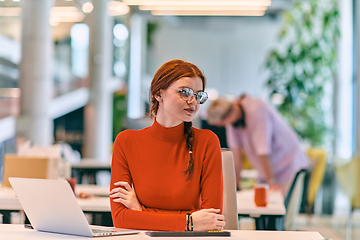 Image showing In a modern startup office, a professional businesswoman with orange hair sitting at her laptop, epitomizing innovation and productivity in her contemporary workspace.