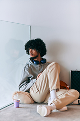 Image showing African-American entrepreneur taking a relaxing break from work, sitting on the floor while using wireless headphones and a smartphone for some digital entertainment.