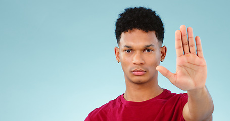 Image showing Man, hand and stop in studio portrait with forbidden warning, rejection and negative by blue background. Face, palm and hand gesture for defence sign or no, deny and wait for frustrated in mockup