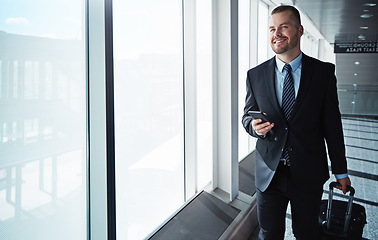 Image showing Business man, smartphone and window in airport hallway with smile, thinking and vision on international travel. Entrepreneur, luggage and phone with flight schedule for global immigration in London