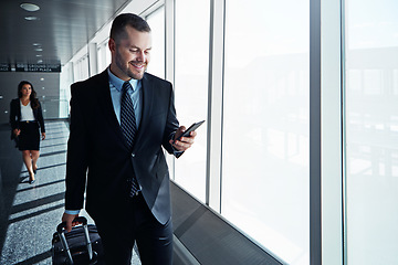 Image showing Business man, phone and travel in airport window for reading, thinking and contact in corridor with smile. Entrepreneur, luggage and smartphone for flight schedule and global immigration in London