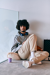 Image showing African-American entrepreneur taking a relaxing break from work, sitting on the floor while using wireless headphones and a smartphone for some digital entertainment.