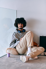 Image showing African-American entrepreneur taking a relaxing break from work, sitting on the floor while using wireless headphones and a smartphone for some digital entertainment.