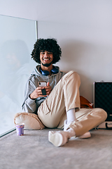 Image showing African-American entrepreneur taking a relaxing break from work, sitting on the floor while using wireless headphones and a smartphone for some digital entertainment.