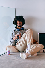 Image showing African-American entrepreneur taking a relaxing break from work, sitting on the floor while using wireless headphones and a smartphone for some digital entertainment.