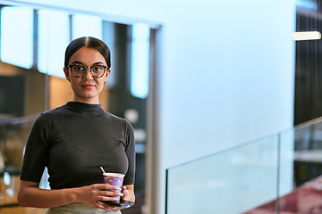 Image showing In a bustling modern office a businesswoman in glasses juggles her tasks, sipping coffee and using her smartphone, epitomizing the dynamic and multitasking nature of contemporary corporate life