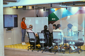 Image showing A pregnant business woman with orange hair confidently presents her business plan to colleagues in a modern glass office, embodying entrepreneurship and innovation