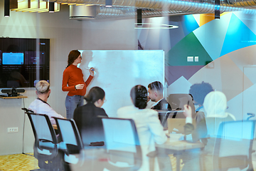 Image showing A pregnant business woman with orange hair confidently presents her business plan to colleagues in a modern glass office, embodying entrepreneurship and innovation