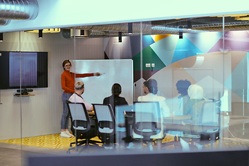 Image showing A pregnant business woman with orange hair confidently presents her business plan to colleagues in a modern glass office, embodying entrepreneurship and innovation