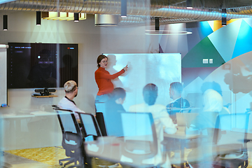 Image showing A pregnant business woman with orange hair confidently presents her business plan to colleagues in a modern glass office, embodying entrepreneurship and innovation