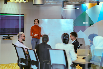 Image showing A pregnant business woman with orange hair confidently presents her business plan to colleagues in a modern glass office, embodying entrepreneurship and innovation