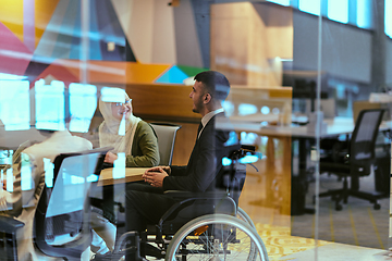 Image showing In a modern glass startup office, a wheelchair-bound director leads a successful meeting with colleagues, embodying inclusivity and teamwork.