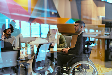 Image showing In a modern glass startup office, a wheelchair-bound director leads a successful meeting with colleagues, embodying inclusivity and teamwork.