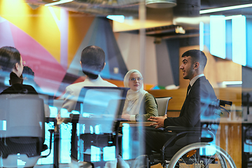 Image showing In a modern glass startup office, a wheelchair-bound director leads a successful meeting with colleagues, embodying inclusivity and teamwork.