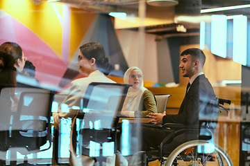 Image showing In a modern glass startup office, a wheelchair-bound director leads a successful meeting with colleagues, embodying inclusivity and teamwork.