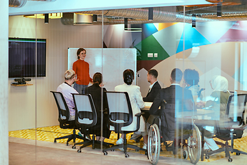 Image showing A pregnant business woman with orange hair confidently presents her business plan to colleagues in a modern glass office, embodying entrepreneurship and innovation