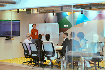 Image showing A pregnant business woman with orange hair confidently presents her business plan to colleagues in a modern glass office, embodying entrepreneurship and innovation