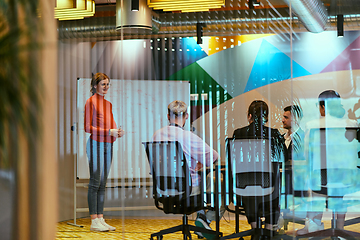 Image showing A pregnant business woman with orange hair confidently presents her business plan to colleagues in a modern glass office, embodying entrepreneurship and innovation