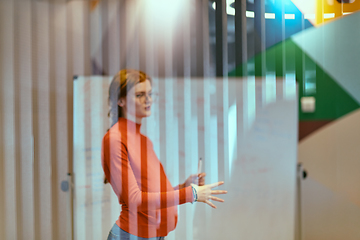 Image showing A pregnant business woman with orange hair confidently presents her business plan to colleagues in a modern glass office, embodying entrepreneurship and innovation