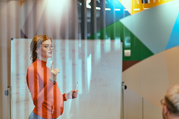 Image showing A pregnant business woman with orange hair confidently presents her business plan to colleagues in a modern glass office, embodying entrepreneurship and innovation